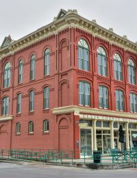 Historic red brick building housing Ellis County Museum, with arched windows and parked cars in front.