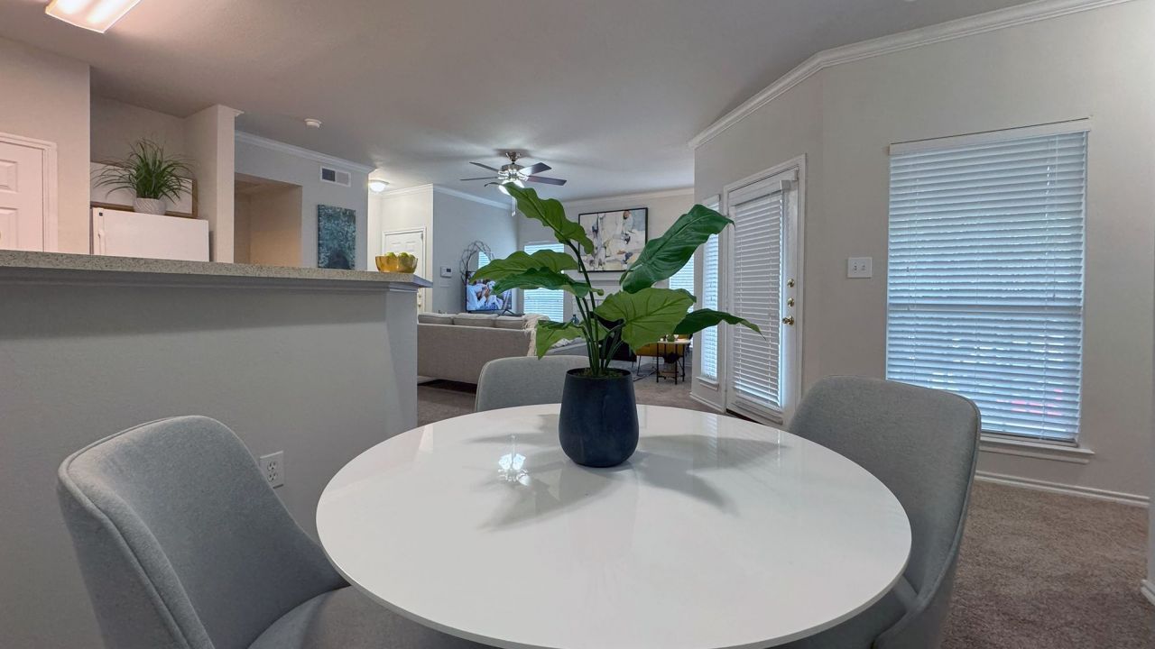 Modern living area with gray chairs at a round white table and a potted plant, leading to a cozy living room.