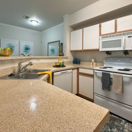 A modern kitchen with beige countertops, white cabinets, an electric stove, and a microwave. Decor accents are visible.