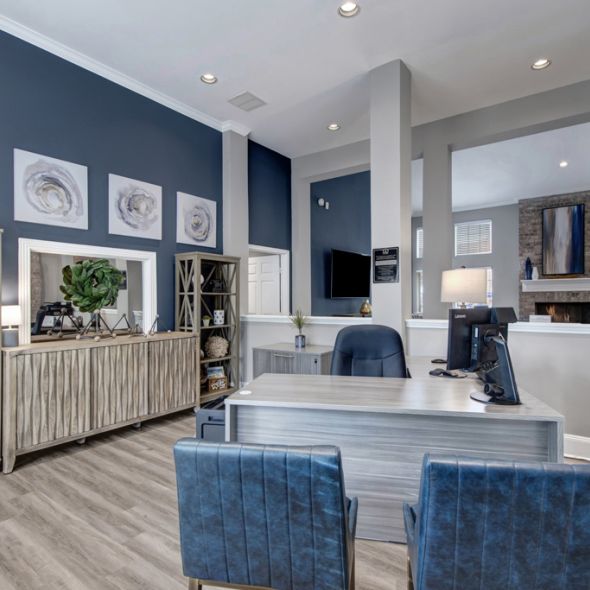 Modern office with blue chairs, desk, shelves, and artwork on blue walls. Brick accent and printer in the background.