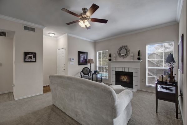 Living room with a beige sofa, ceiling fan, fireplace, and windows letting in natural light.