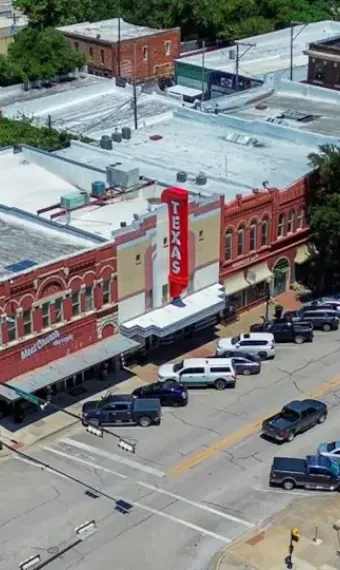 Aerial view of Texas Theater in a historic neighborhood with surrounding parked cars and buildings.